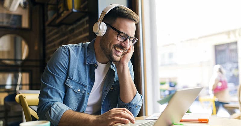 Man dressing casually and listening on headphone while using laptop